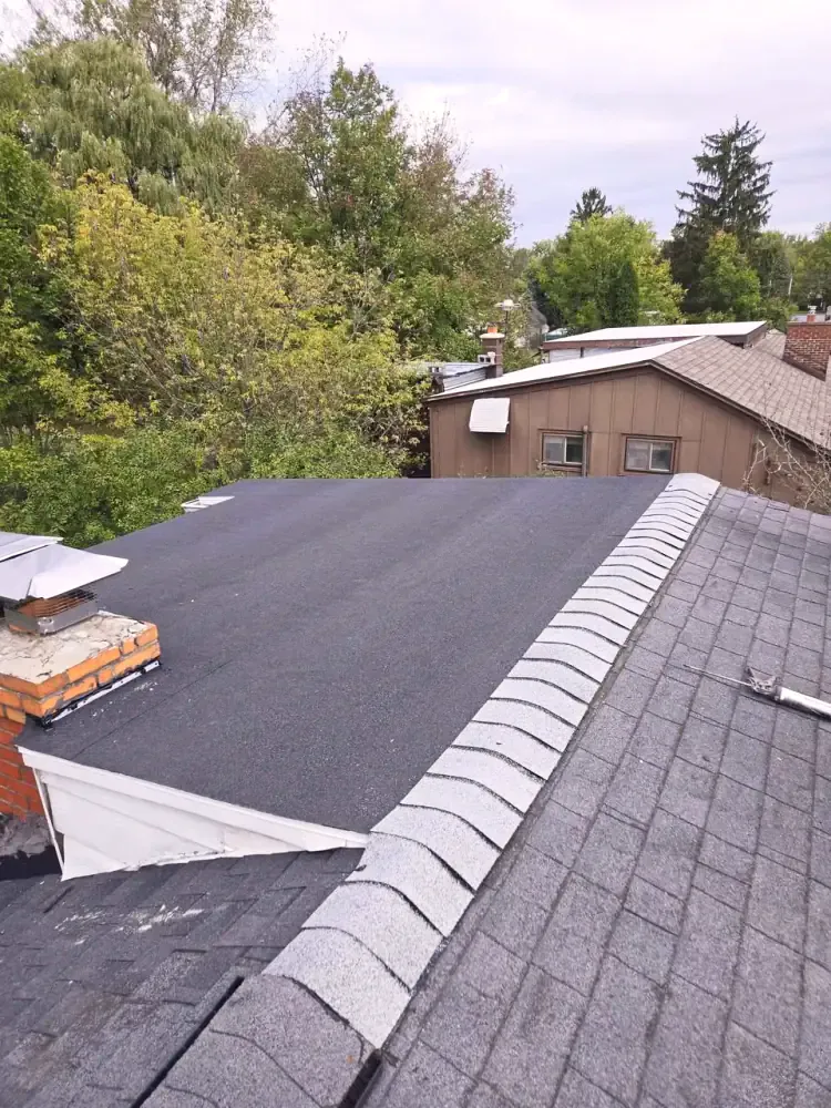 A low-slope flat roof section meeting a pitched asphalt shingle roof beside a brick chimney