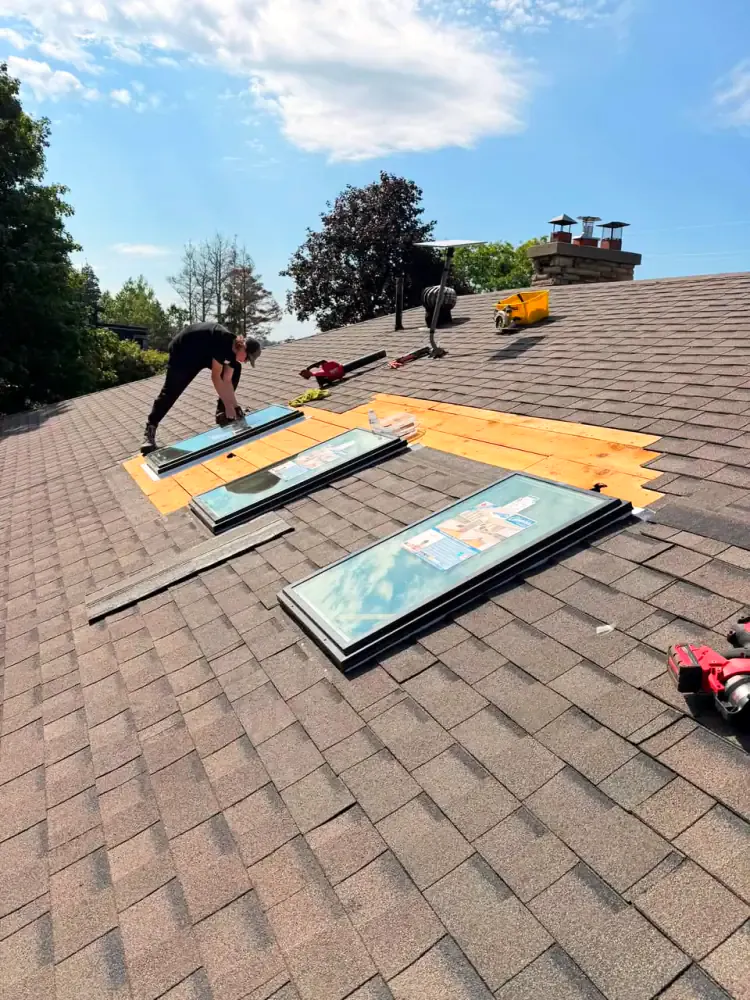 Roofer fitting new skylight units into openings cut in a shingle roof with the decking exposed around them